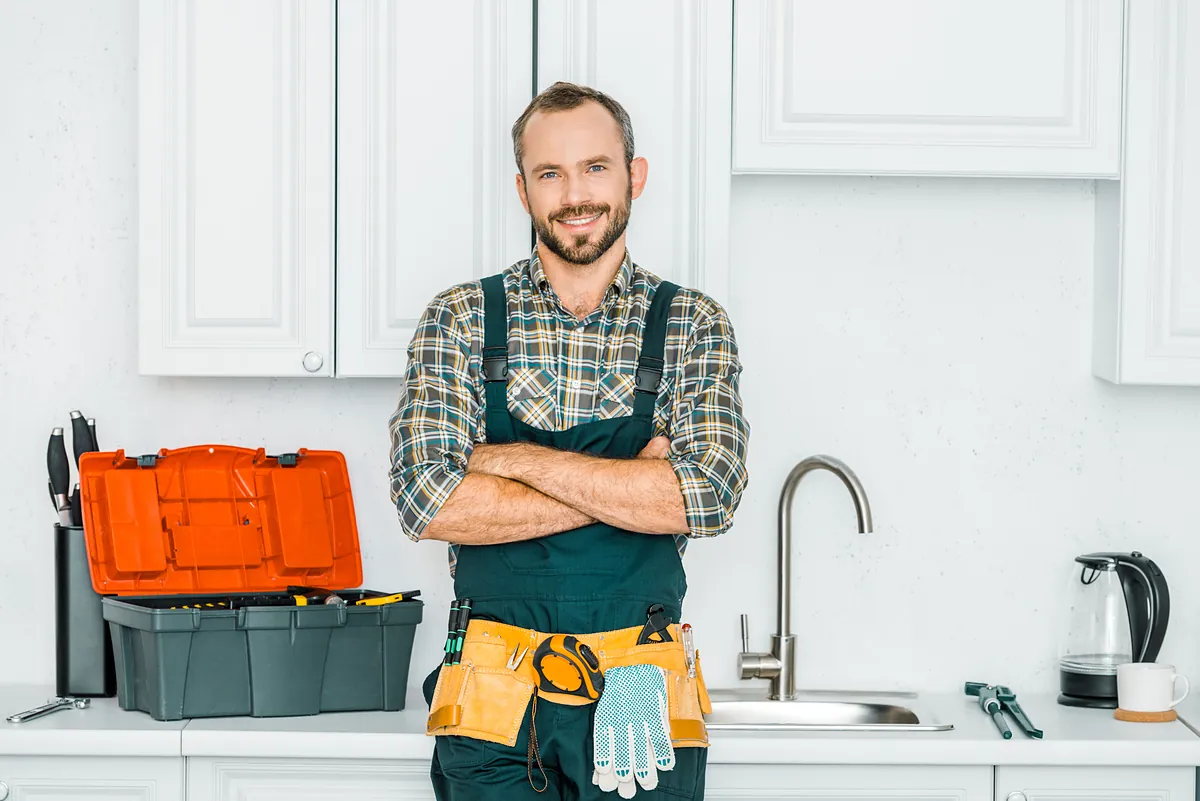 Installateur für Rohrreinigung mit Werkzeugkoffer in der Küche in Planegg Freundlicher Installateur mit Werkzeugkoffer und Werkzeuggürtel in einer Küche – Einsatz in Planegg