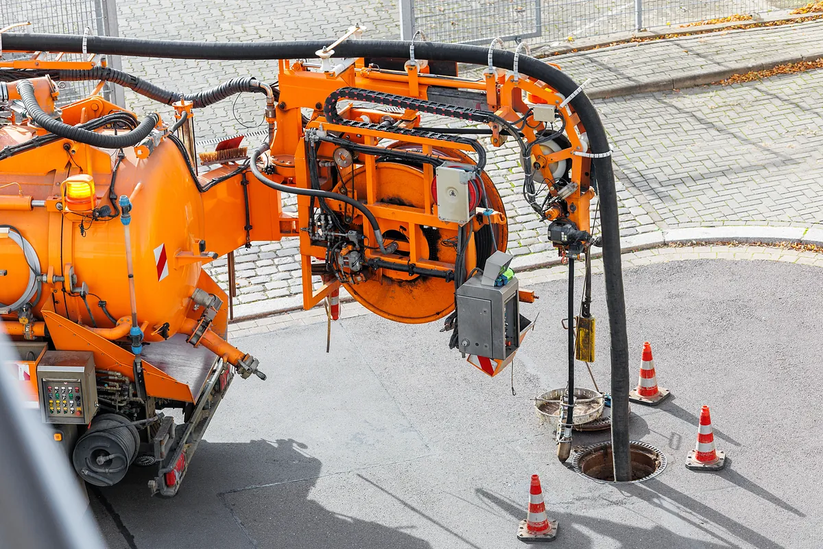 Kanalreinigung mit Saugwagen am Kanalschacht in München und Umgebung Orangefarbener Kanalreinigungswagen saugt an einem geöffneten Kanalschacht auf der Straße – Einsatz in München und Umgebung