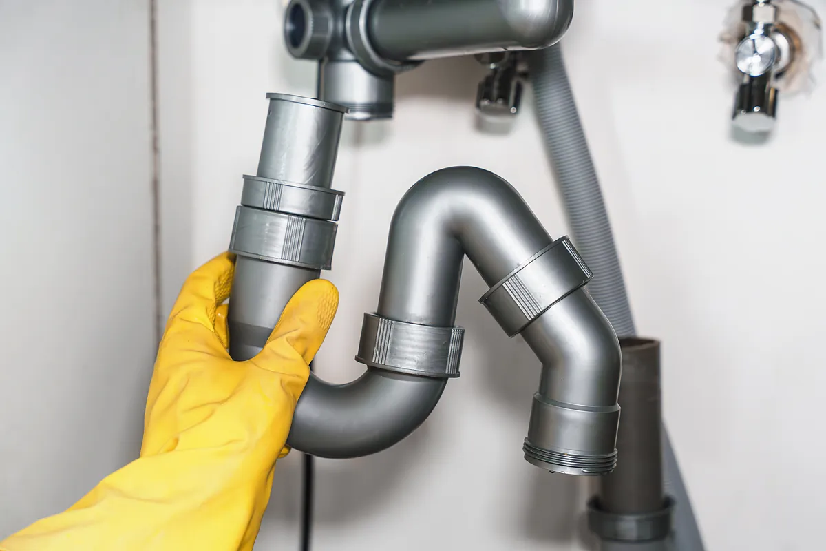 Hand im gelben Handschuh öffnet den Siphon unter einem Waschbecken – Einsatz in Eichenau